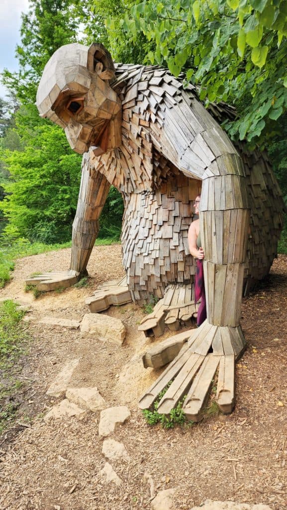 A woman pokes her head out from behind the arm of a giant troll sculpture.