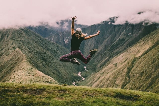 Woman jumping for joy on a mountain top because she receives unique travel gifts for women.