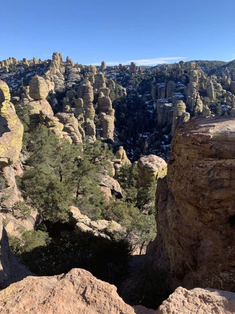 Stacks of snow capped boulders protrude through the air against a blue sky. Chiricahua National Monument is one of the best peak hikes near Tucson.