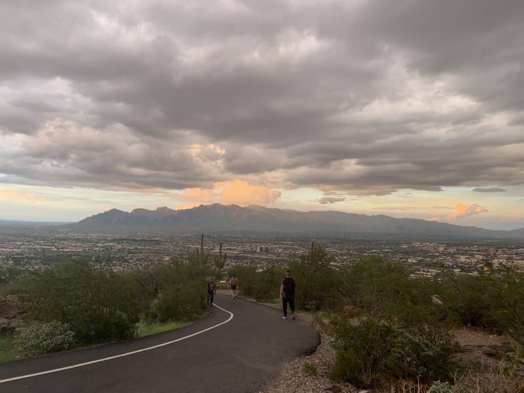 A cloudy sky looms over a paved hiking trail in the desert. Tumamoc is one of the best peak hikes near Tucson.