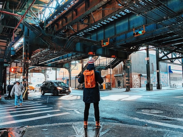 A person stands at a cross walk wearing a backpack