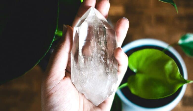 A hand holds a clear quartz crystal