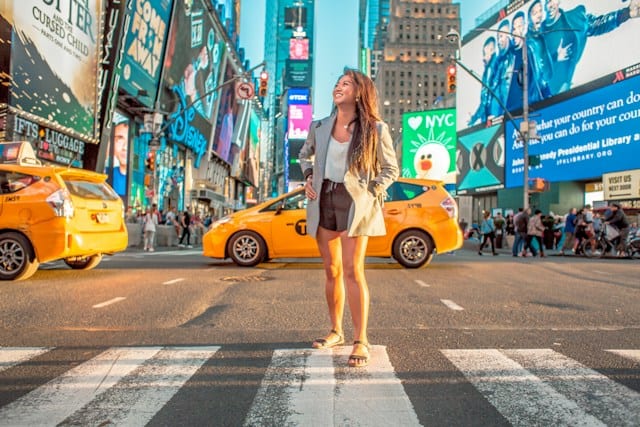 A woman stands on a crosswalk on a street in a bustling city.