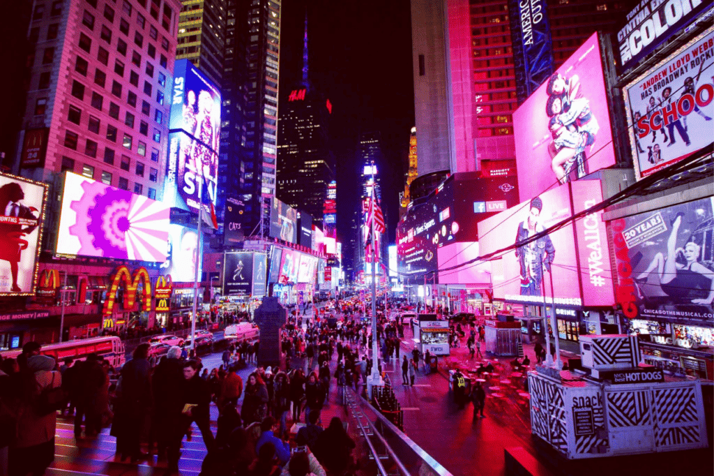 A crowded street at night lit up with the lights from glowing billboards.