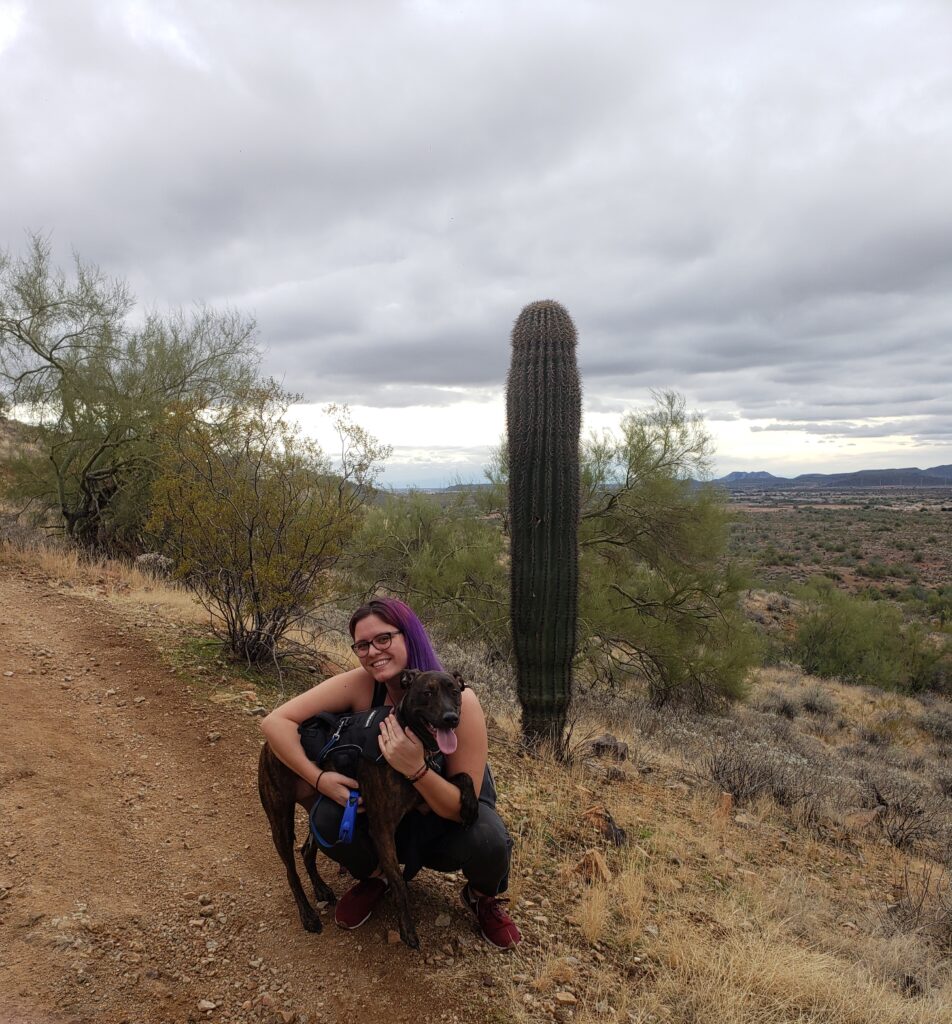 A woman and a dog pose for a picture in front of a cactus.
