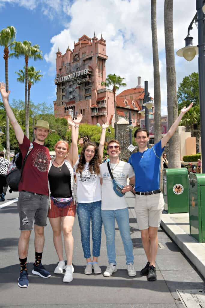 A group of people pose with their arms raised in front of Tower of Terror, one of the best photo spots at Hollywood Studios.