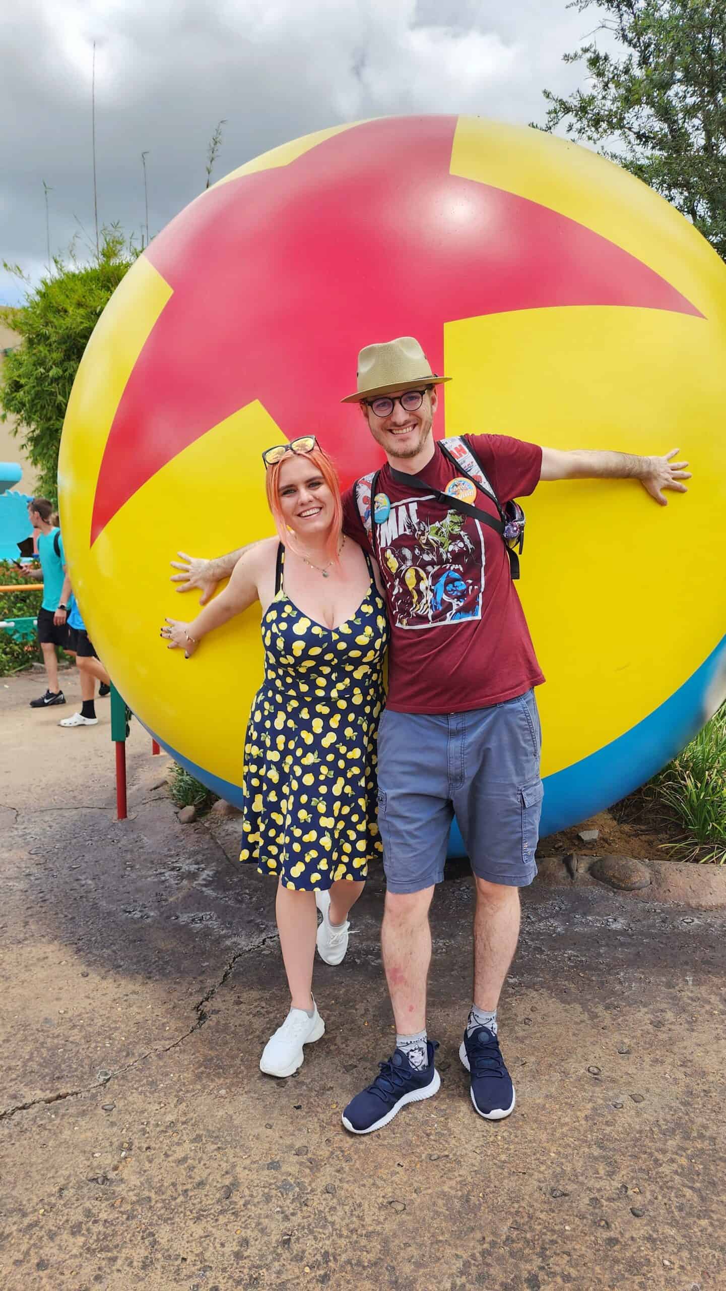 A woman and a man pretend to hold a giant ball sculpture on their backs.