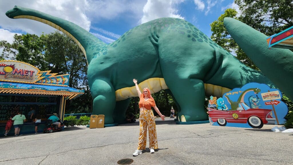 A woman stands in front of a giant long necked dinosaur statue.