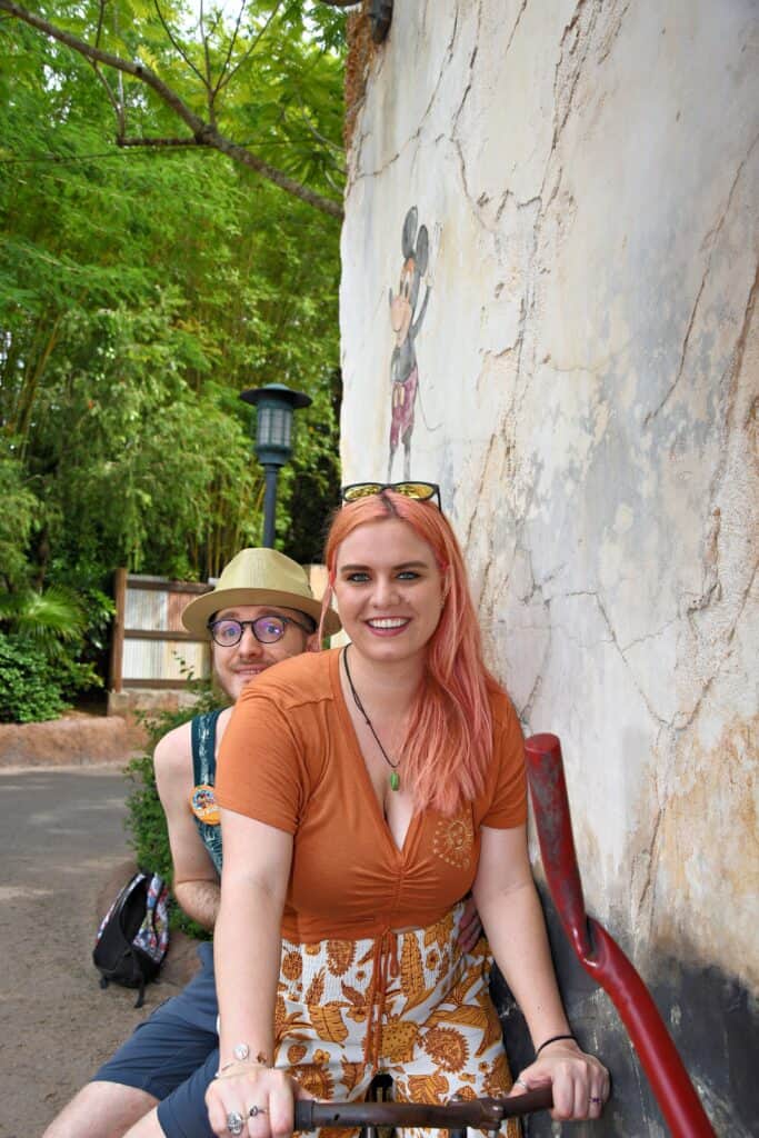 A woman sits on a bike and a man rides behind her.