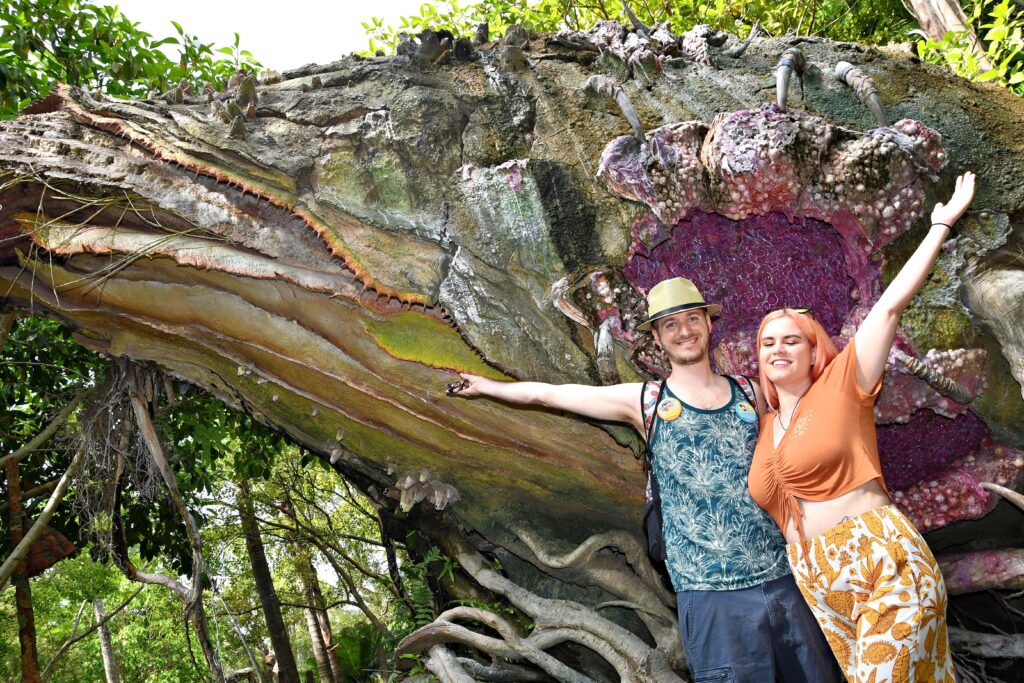 A woman and man stand in front of a large jungle plant sculpture.