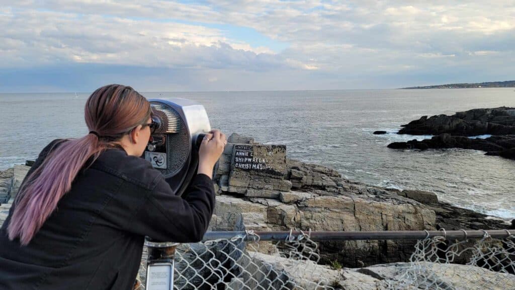 A woman peers through binoculars at the ocean.