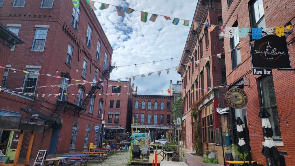 A group of brick buildings form a colorful square where flags are strung from each structure.