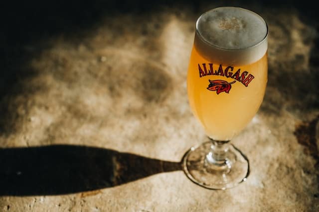 A glass of beer with the word "Allagash" printed on it.