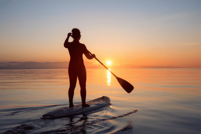 A woman paddle boards at sunset