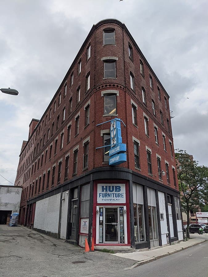 An old red brick building standing five stories high with a sign that says, "Hub Furniture Company."