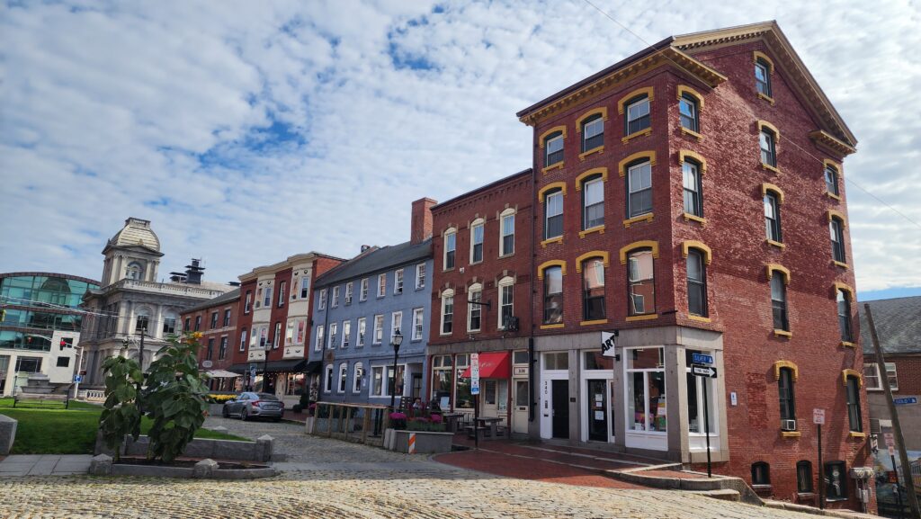 A row of historic brick buildings set on top of a cobblestone streeet.