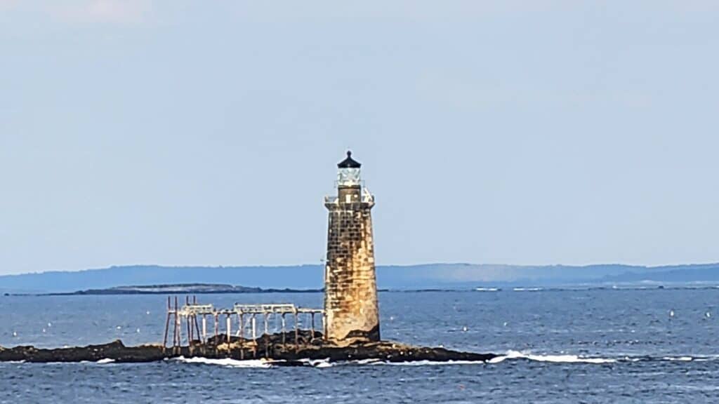 A lighthouse stands alone on a tiny island out at sea.
