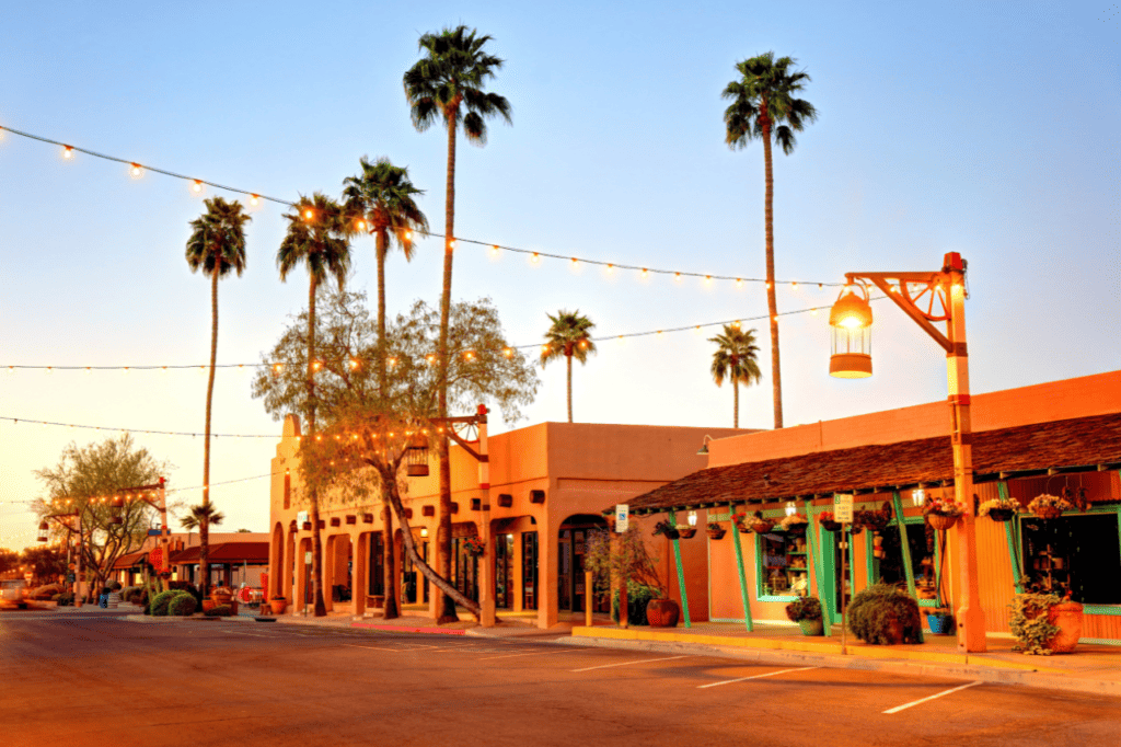 A southwestern shopping center adorned with bulb lights and palm trees at sunset.