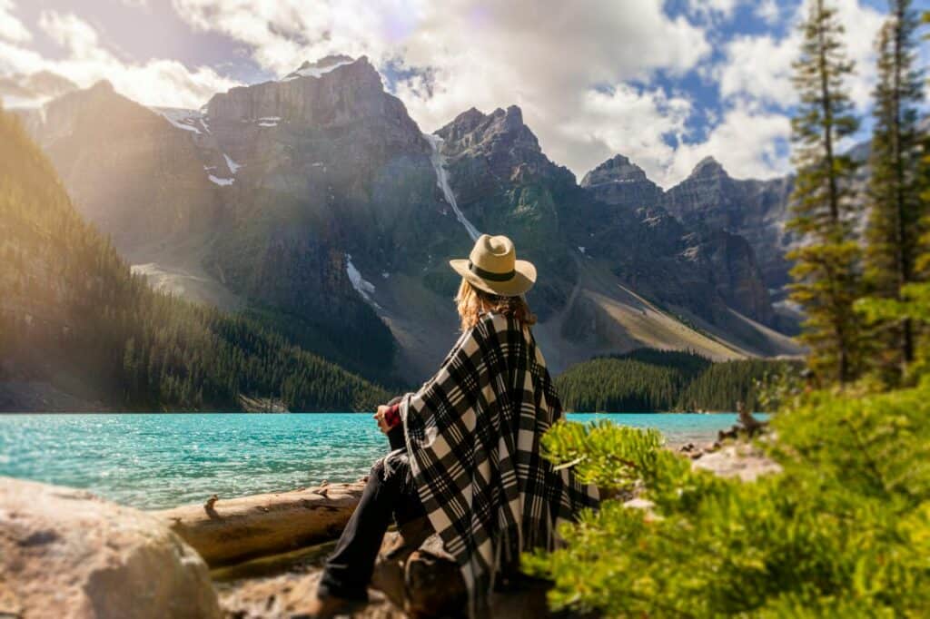 A woman sits on a rock looking over a lake to towering mountain peaks