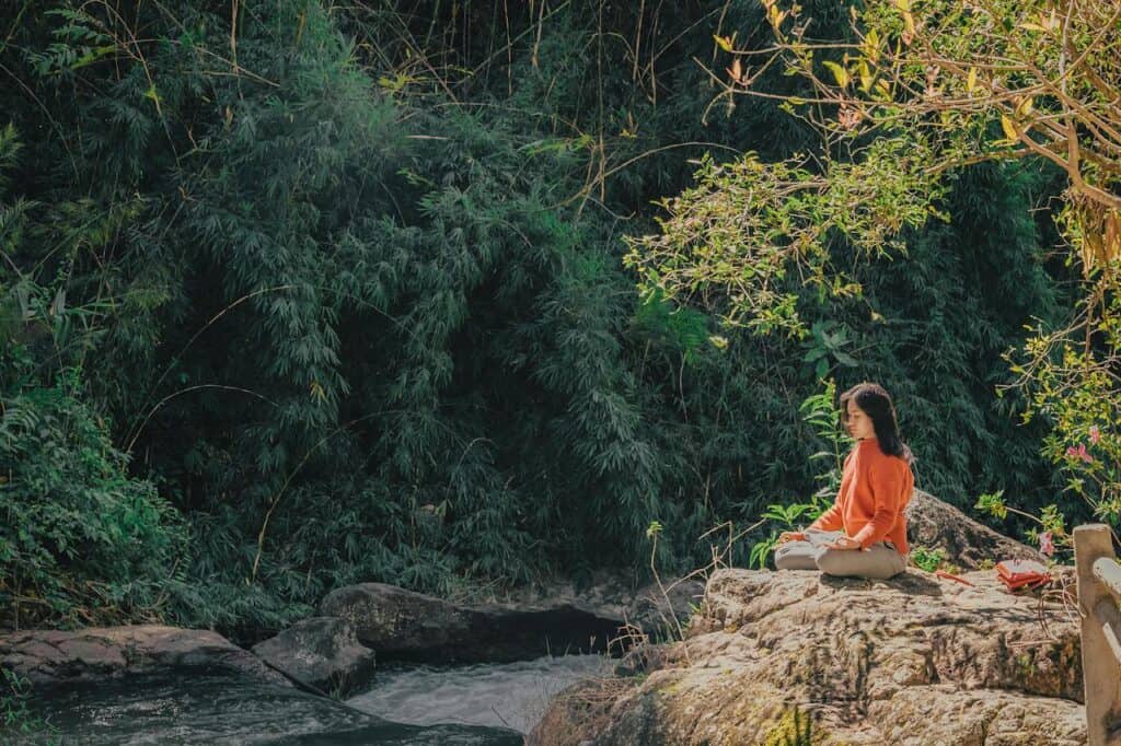 a woman sits in meditation on a rock in nature