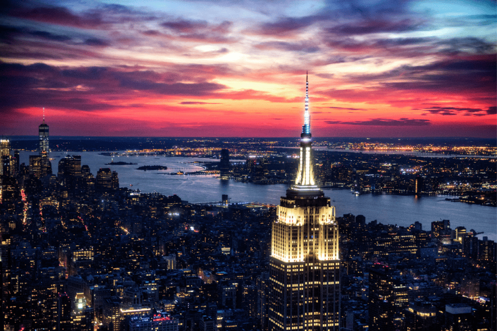 The top of a skyscraper is lit up against a city skyline at dusk.