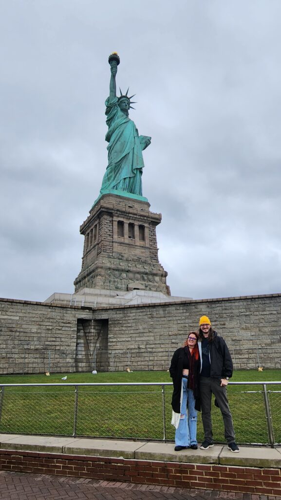 A couple stands at the base of the Statue of Liberty.