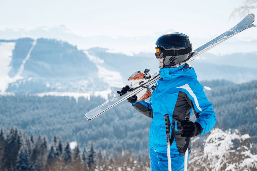 A woman in a blue snowsuit holds her skis over her shoulders on a mountain