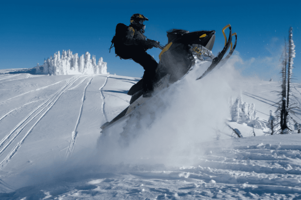 A person in a snowsuit and helmet do a trick on a snowmobile.