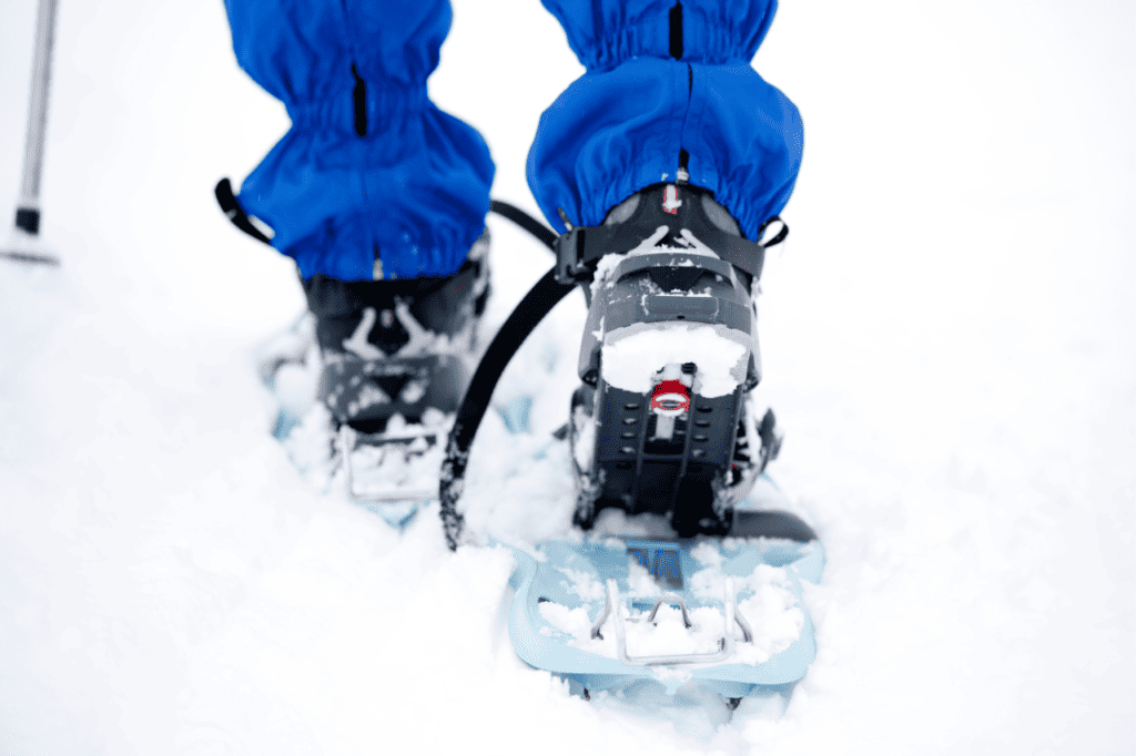A person in a bright blue snowsuit snowshoes through the snow.