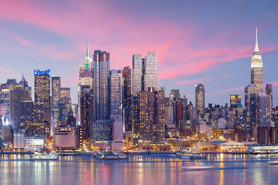 The New York City skyline is bathed in purple and pink at sunset.