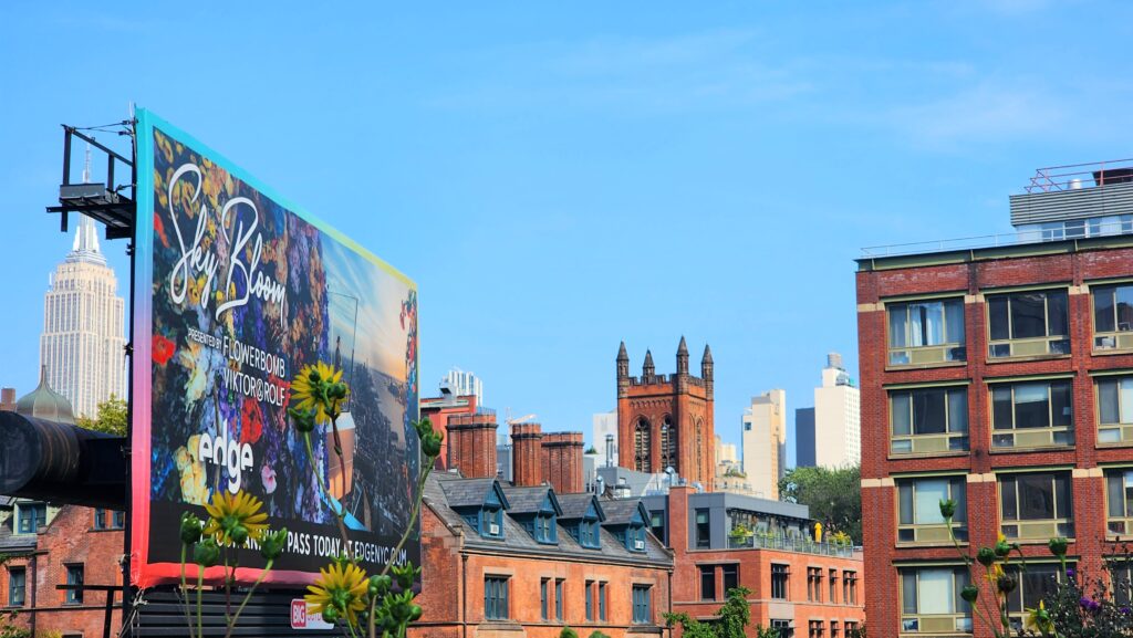 A colorful billboard is in the foreground of a cluster of red brick buildings. 