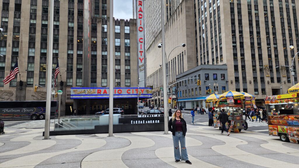 A woman stands in front of Radio City Music Hall. The street is almost empty.